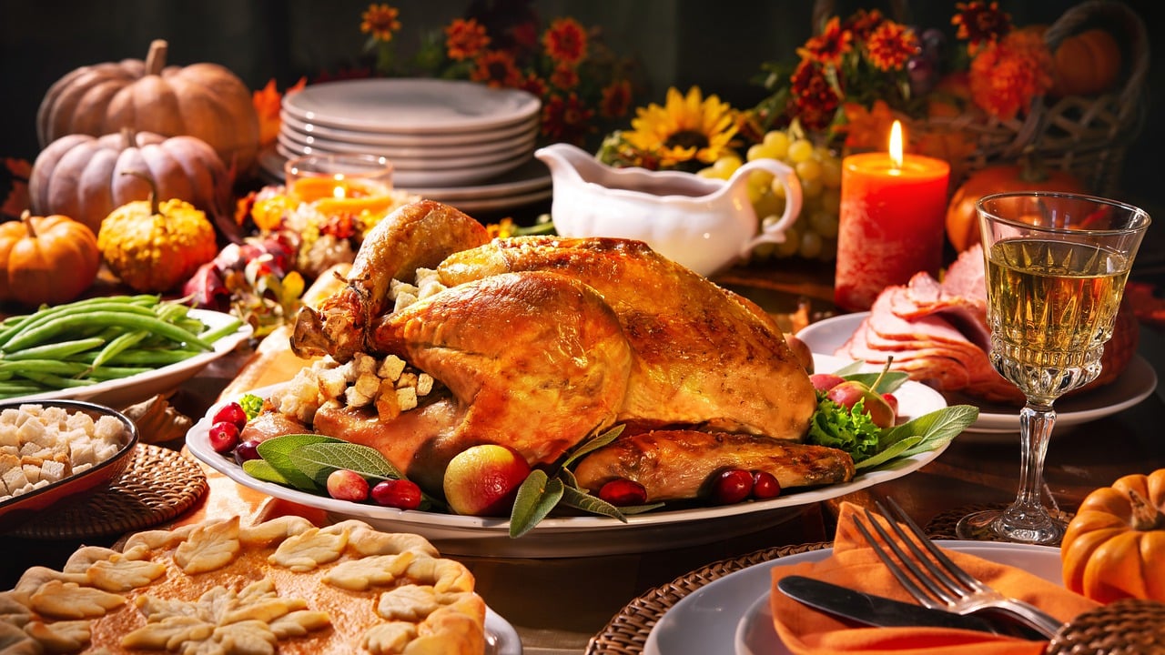 Holiday meal setting that includes a turnkey, green beans, apple pie, ham, gravy, stuffing, decorations and tableware.